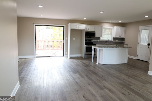 kitchen with a kitchen breakfast bar, dark stone counters, stainless steel appliances, wood-type flooring, and white cabinets