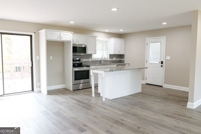 kitchen with a center island, light hardwood / wood-style flooring, light stone countertops, appliances with stainless steel finishes, and white cabinetry