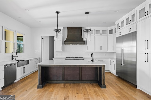 kitchen with sink, black dishwasher, an island with sink, custom range hood, and built in fridge