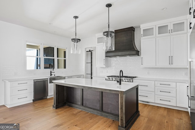 kitchen featuring premium range hood, sink, a kitchen island with sink, and white cabinets