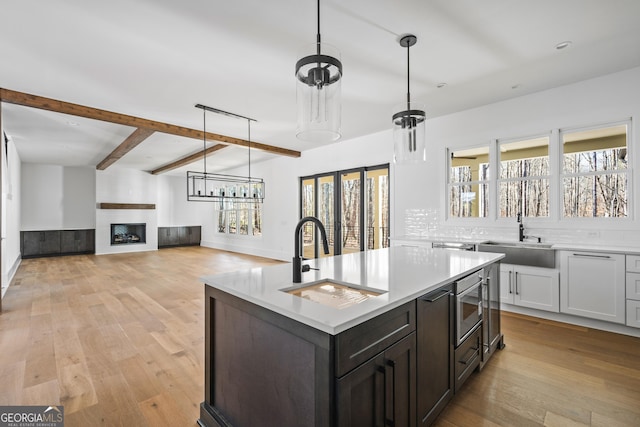 kitchen with sink, light wood-type flooring, a large fireplace, stainless steel microwave, and a kitchen island with sink