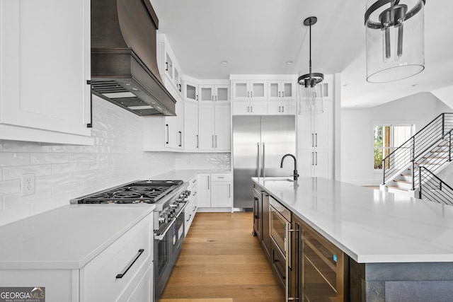 kitchen featuring beverage cooler, a kitchen island with sink, custom range hood, and white cabinets