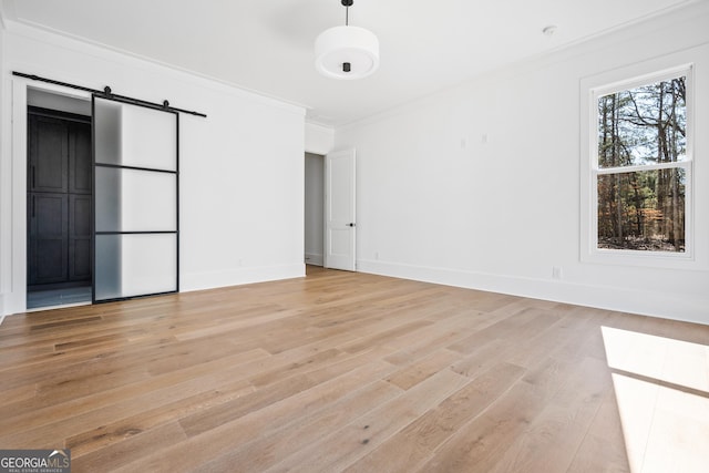 unfurnished room with ornamental molding, a barn door, and light hardwood / wood-style floors