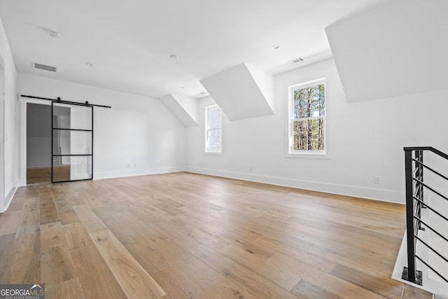 bonus room with a barn door, a healthy amount of sunlight, and light hardwood / wood-style flooring