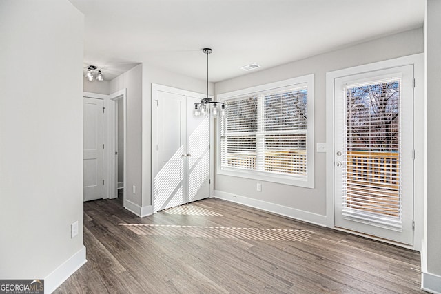 unfurnished dining area featuring a chandelier and dark wood-type flooring