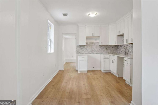 kitchen with white cabinets, decorative backsplash, light wood-type flooring, and sink