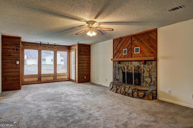 unfurnished living room with a textured ceiling, a fireplace, visible vents, and carpet flooring