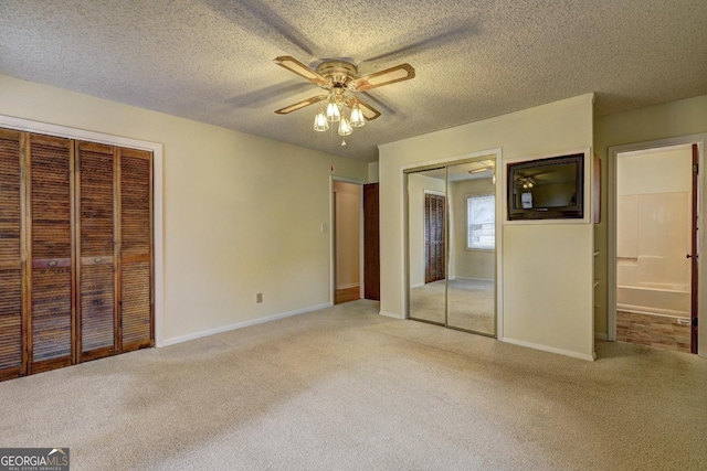 unfurnished bedroom with light colored carpet, a textured ceiling, baseboards, and two closets