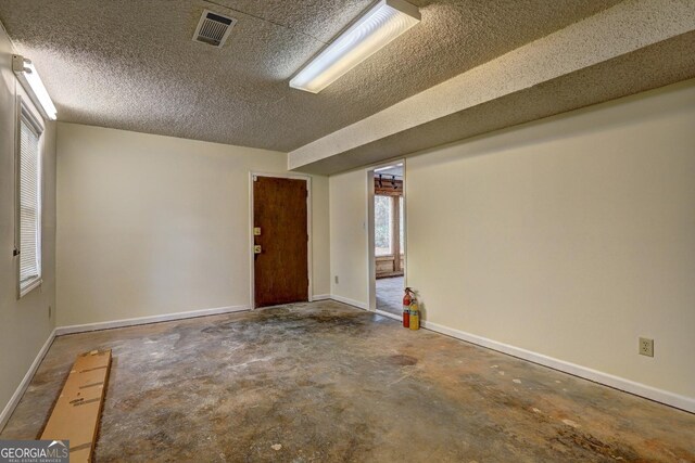 empty room with concrete flooring, visible vents, a textured ceiling, and baseboards