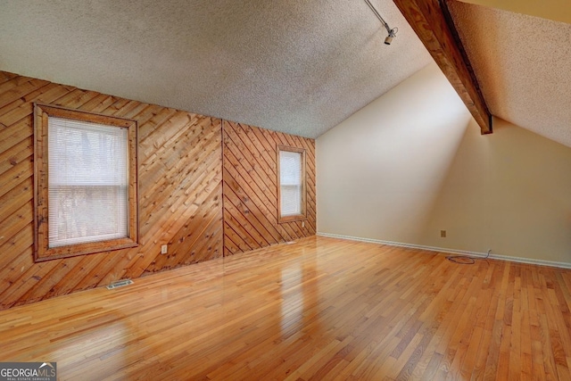 bonus room featuring vaulted ceiling with beams, a textured ceiling, wood walls, wood finished floors, and visible vents