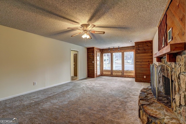 unfurnished living room featuring carpet floors, a stone fireplace, a textured ceiling, and a ceiling fan