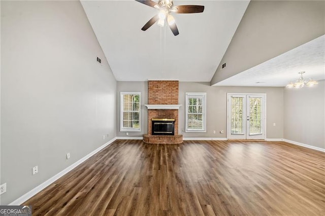 unfurnished living room with ceiling fan with notable chandelier, french doors, hardwood / wood-style flooring, high vaulted ceiling, and a brick fireplace