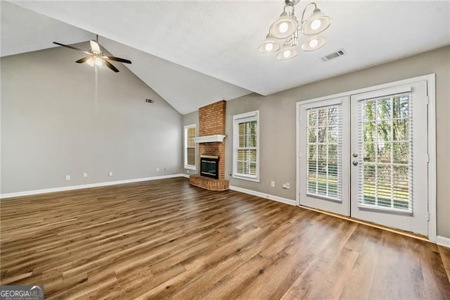 unfurnished living room featuring a brick fireplace, wood-type flooring, lofted ceiling, and ceiling fan with notable chandelier