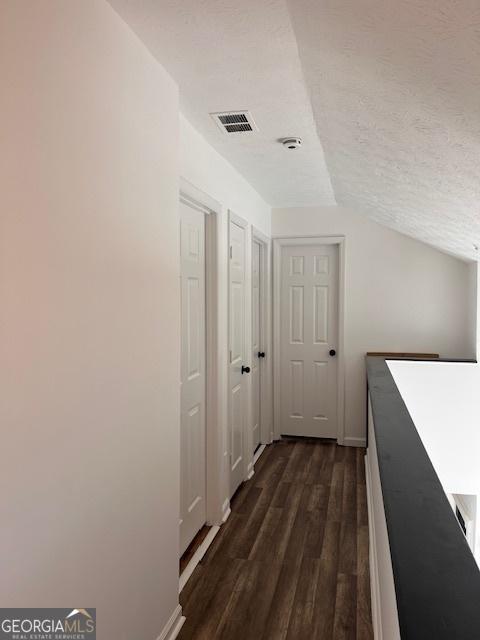 hallway featuring lofted ceiling, dark hardwood / wood-style flooring, and a textured ceiling