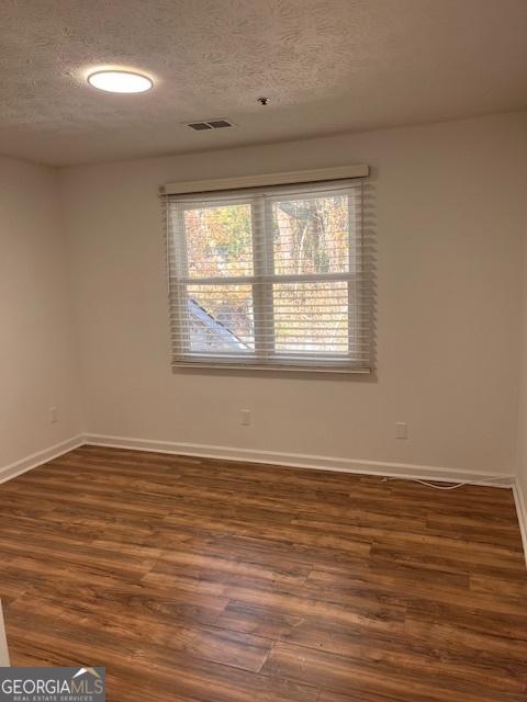 spare room featuring dark wood-type flooring and a textured ceiling