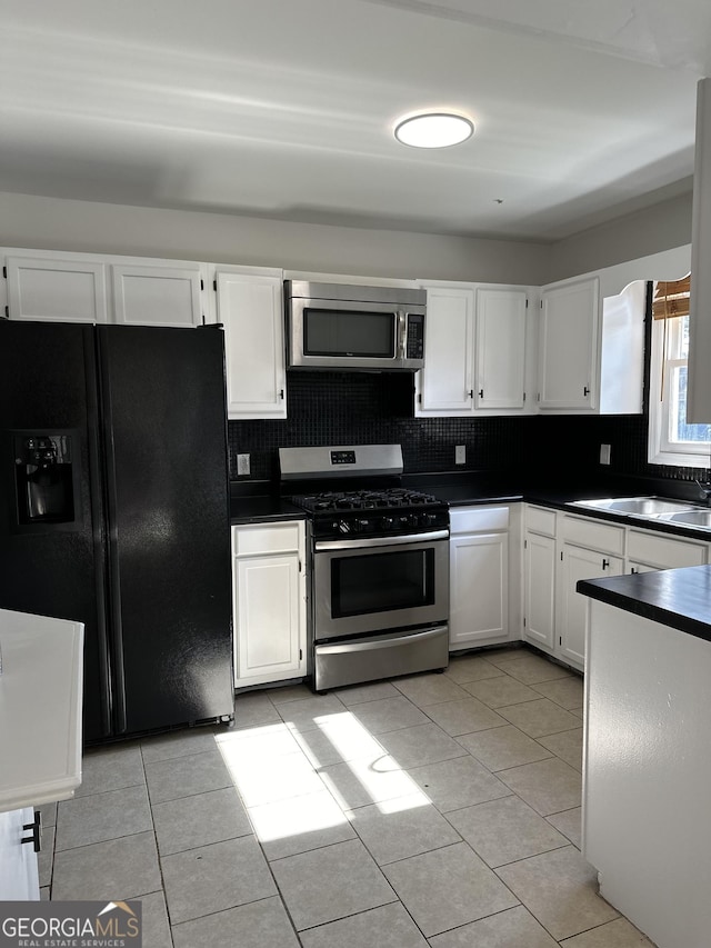 2254 Wellington Cir, Lithonia, GA 30058 - kitchen with appliances with stainless steel finishes, dark countertops, white cabinetry, backsplash, and light tile patterned floors