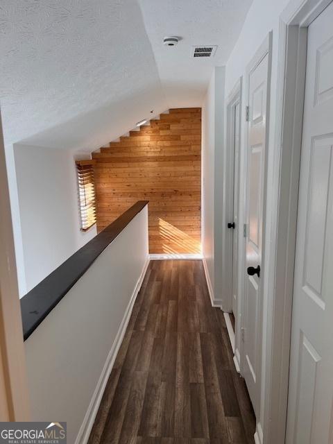 hallway featuring vaulted ceiling, dark hardwood / wood-style floors, a textured ceiling, and wood walls