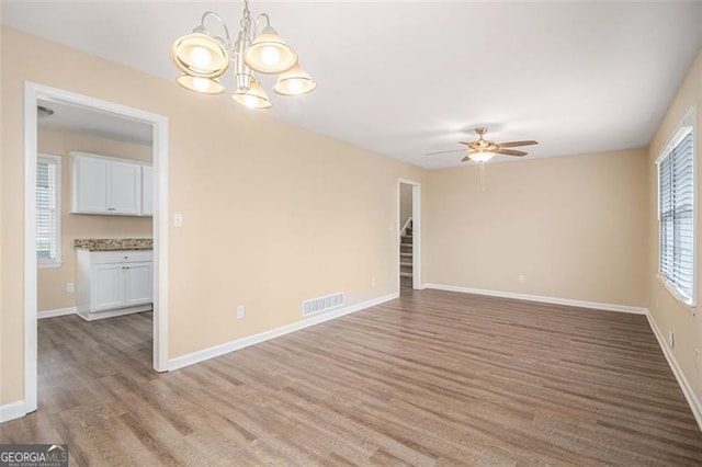 empty room featuring ceiling fan with notable chandelier and light hardwood / wood-style flooring