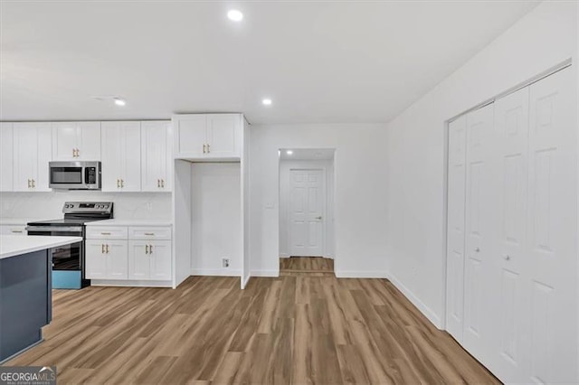 kitchen featuring light wood-type flooring, appliances with stainless steel finishes, decorative backsplash, and white cabinetry