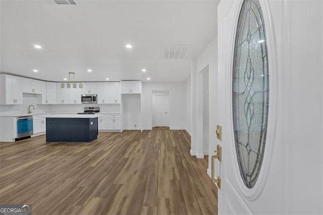 kitchen with a kitchen island, white cabinetry, hardwood / wood-style flooring, hanging light fixtures, and stainless steel appliances