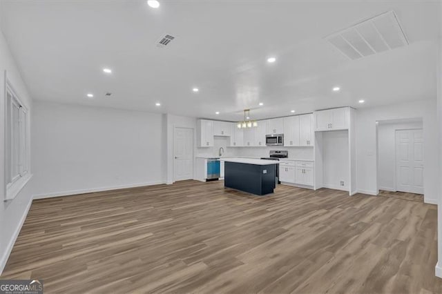 kitchen featuring a center island, white cabinetry, stainless steel appliances, light hardwood / wood-style floors, and hanging light fixtures