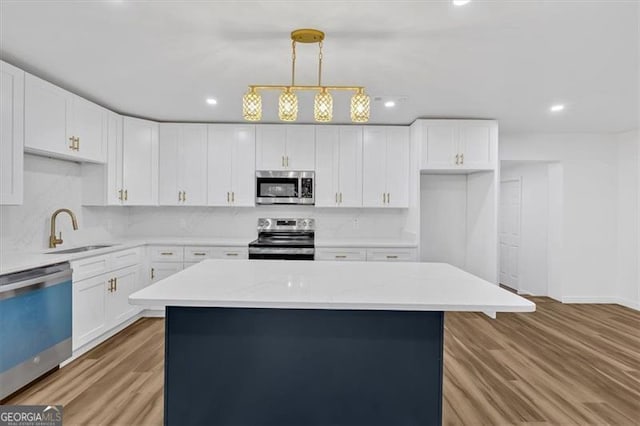 kitchen with appliances with stainless steel finishes, a kitchen island, pendant lighting, white cabinets, and sink