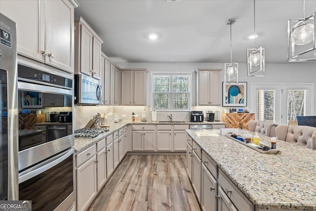 kitchen with light stone counters, stainless steel appliances, and decorative light fixtures