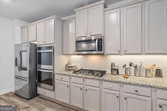 kitchen with light stone countertops, appliances with stainless steel finishes, decorative backsplash, light hardwood / wood-style floors, and white cabinetry