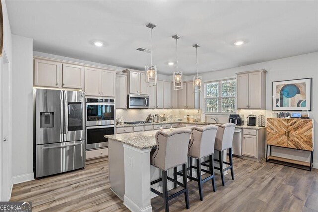 kitchen featuring stainless steel appliances, a kitchen breakfast bar, light stone counters, pendant lighting, and a kitchen island