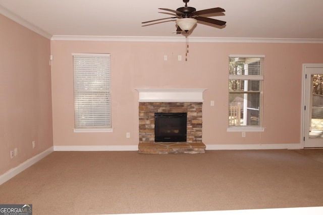 unfurnished living room featuring a stone fireplace, ceiling fan, crown molding, and carpet