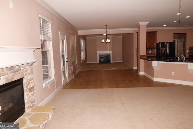 unfurnished living room with dark colored carpet, a stone fireplace, crown molding, and a chandelier