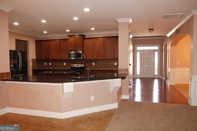 kitchen with sink, stainless steel appliances, kitchen peninsula, dark stone counters, and ornamental molding