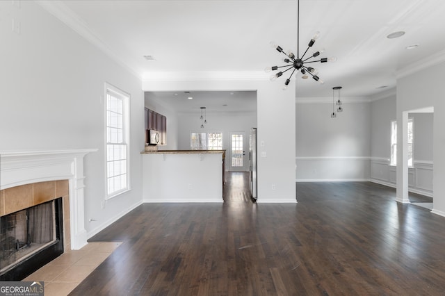 unfurnished living room with a tile fireplace, crown molding, dark wood-type flooring, and a notable chandelier