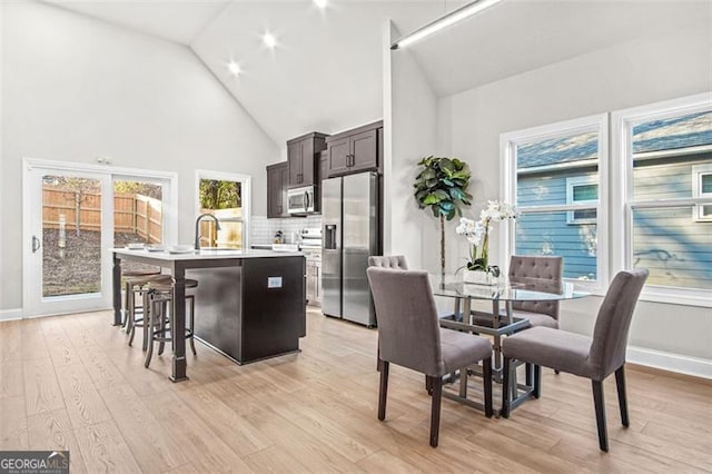 dining area featuring sink, high vaulted ceiling, and light hardwood / wood-style flooring