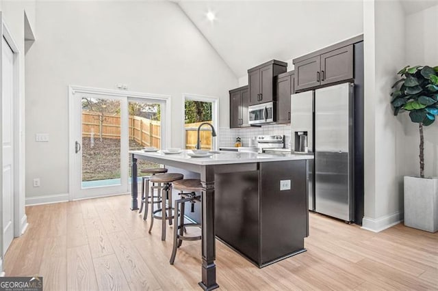 kitchen featuring light hardwood / wood-style flooring, dark brown cabinets, stainless steel appliances, a center island with sink, and a kitchen bar