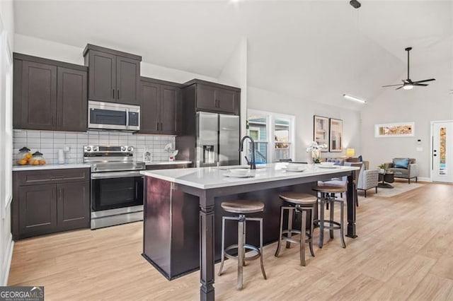 kitchen featuring sink, appliances with stainless steel finishes, a kitchen breakfast bar, light hardwood / wood-style floors, and a center island with sink