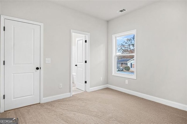 unfurnished bedroom featuring light colored carpet and ensuite bath