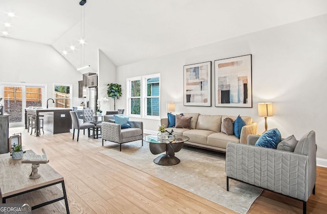 living room with sink, high vaulted ceiling, and light wood-type flooring