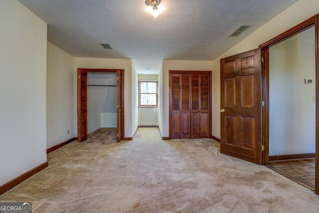 unfurnished bedroom with a textured ceiling, light carpet, and two closets