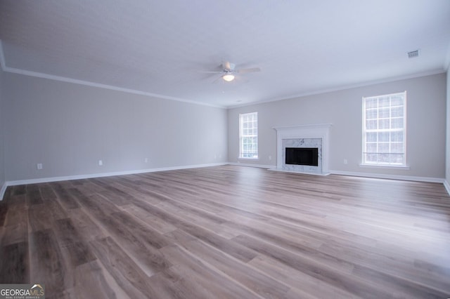 unfurnished living room featuring ceiling fan, wood-type flooring, crown molding, and a high end fireplace