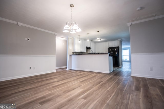 kitchen with black refrigerator, kitchen peninsula, crown molding, a notable chandelier, and white cabinetry