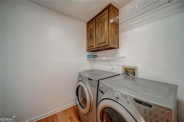 laundry area featuring light wood-type flooring, a textured ceiling, washing machine and dryer, and cabinets