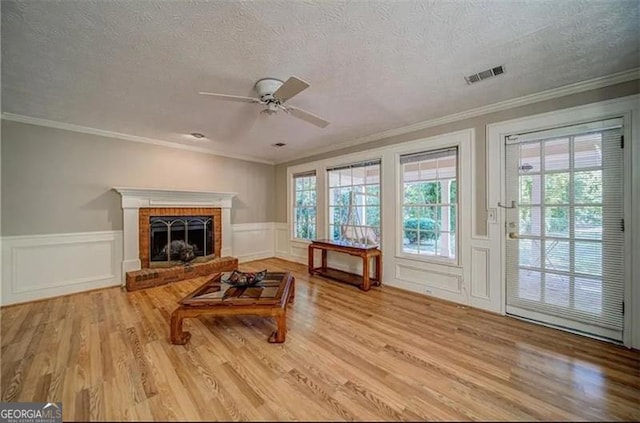 interior space featuring a brick fireplace, light hardwood / wood-style flooring, ceiling fan, and crown molding