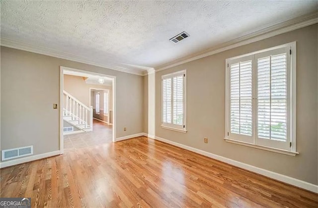 empty room with a textured ceiling, light hardwood / wood-style floors, and crown molding