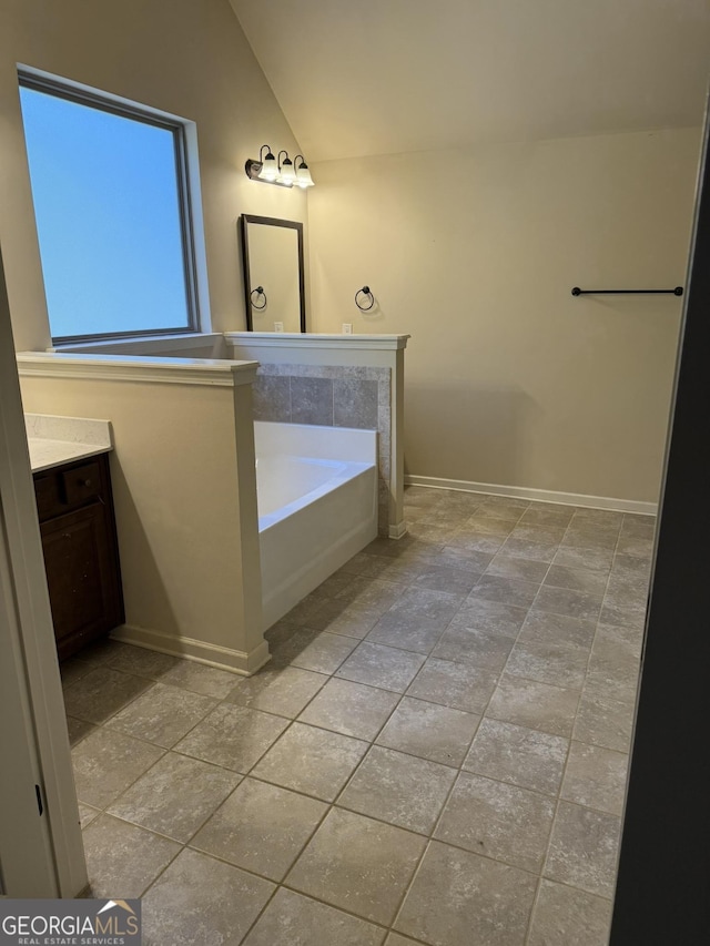 bathroom with a bath, vanity, and lofted ceiling