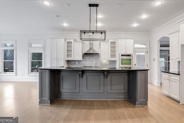 kitchen with white cabinetry, pendant lighting, a large island with sink, and wall chimney range hood