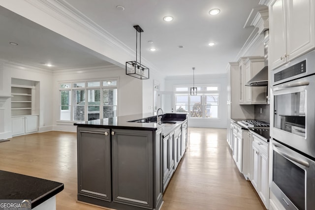 kitchen featuring appliances with stainless steel finishes, decorative light fixtures, white cabinetry, a kitchen island with sink, and light hardwood / wood-style floors