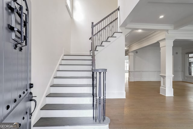 staircase featuring decorative columns, wood-type flooring, and ornamental molding