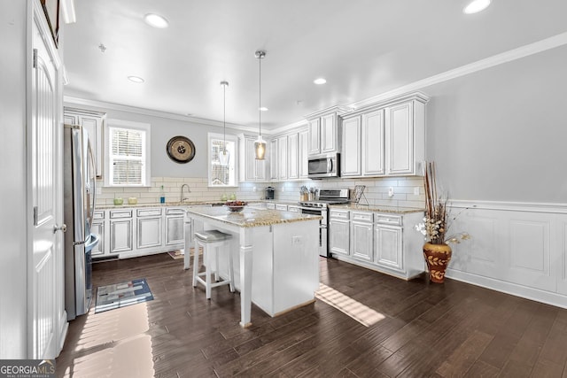 kitchen with dark wood finished floors, stainless steel appliances, ornamental molding, a sink, and a kitchen island