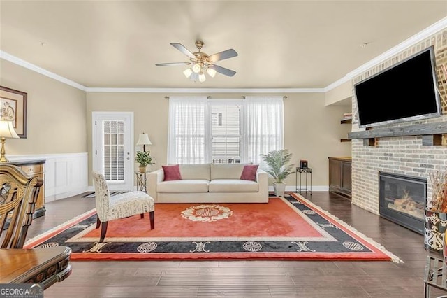 living area with ornamental molding, a fireplace, ceiling fan, and wood finished floors